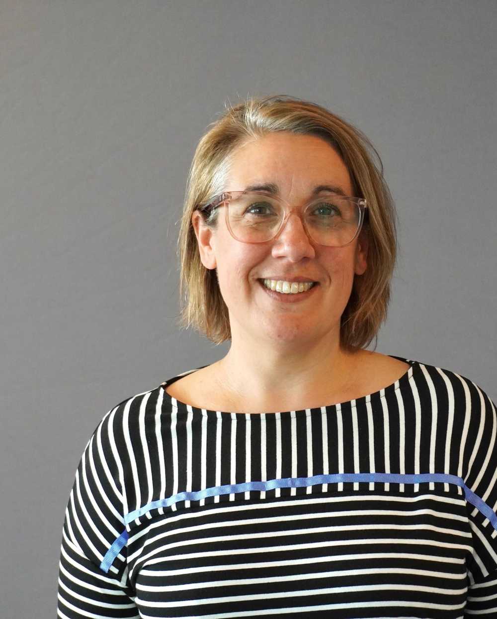 A woman in front of a grey background smiling at the camera